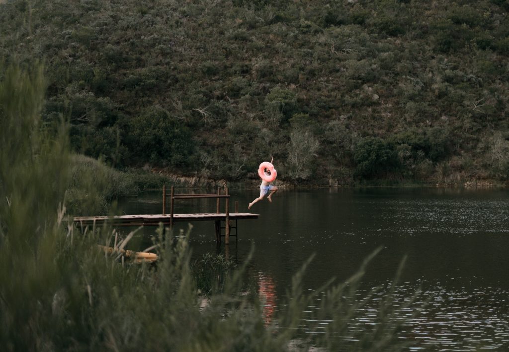 person jumping in lake from pier with life preserver